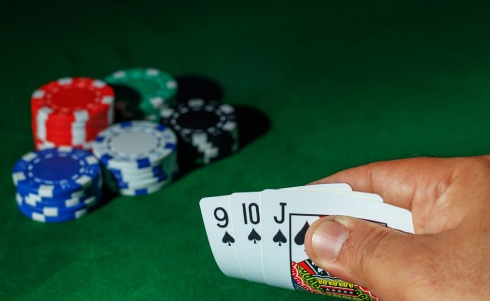 A hand holding playing cards with casino chips on the green felt table.