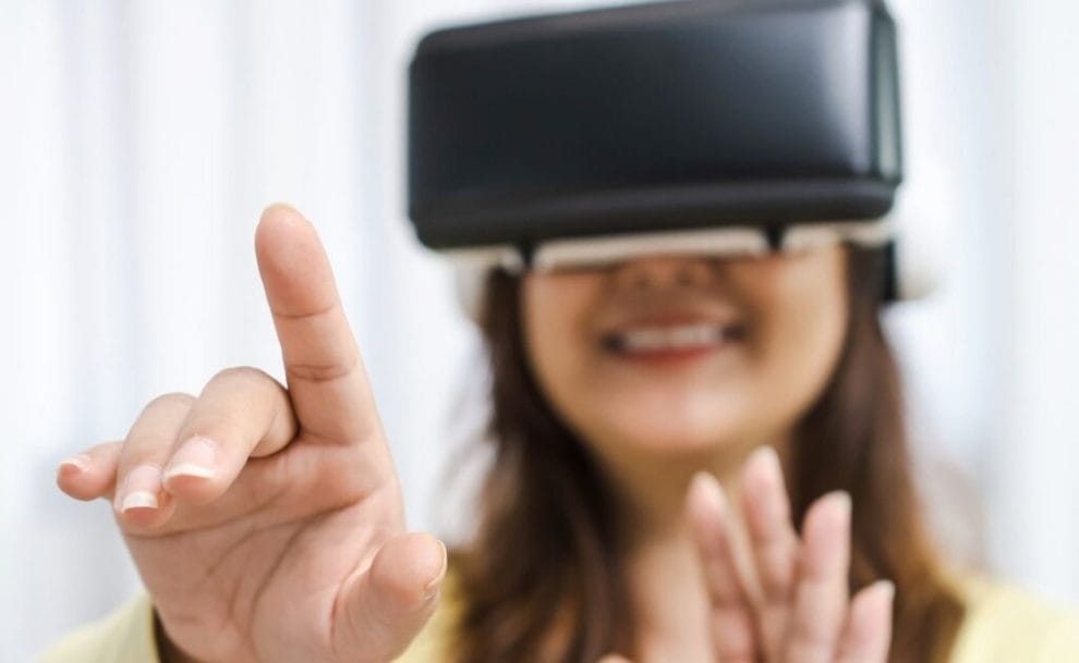 a woman is smiling while wearing a virtual reality headset in the blurred background with her hands coming into focus in the foreground as she points forward