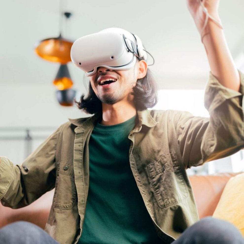 a man is sitting on a couch and cheering while wearing a virtual reality headset