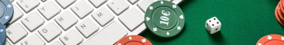 A close up of a computer keyboard, with poker chips and a dice arranged on the table.