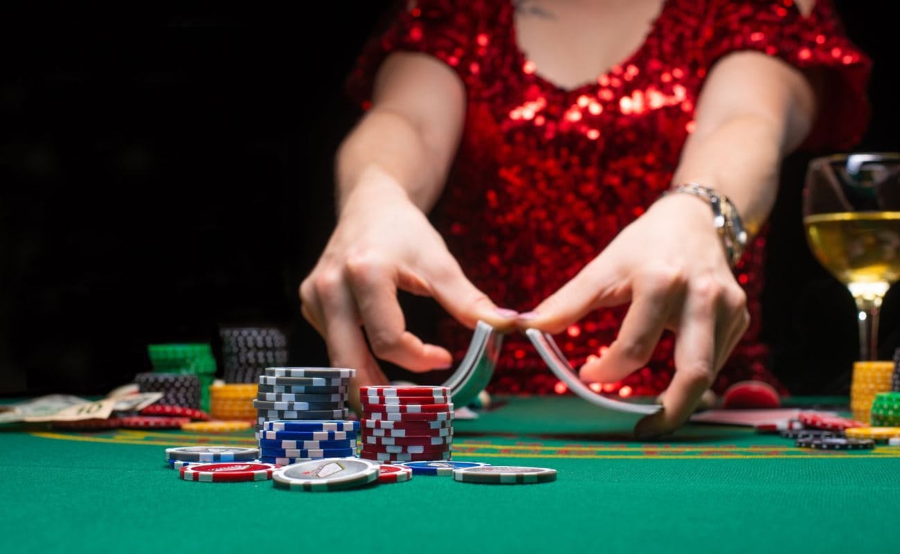 A dealer shuffling cards at a poker table, with casino chips stacked and arranged on the table.