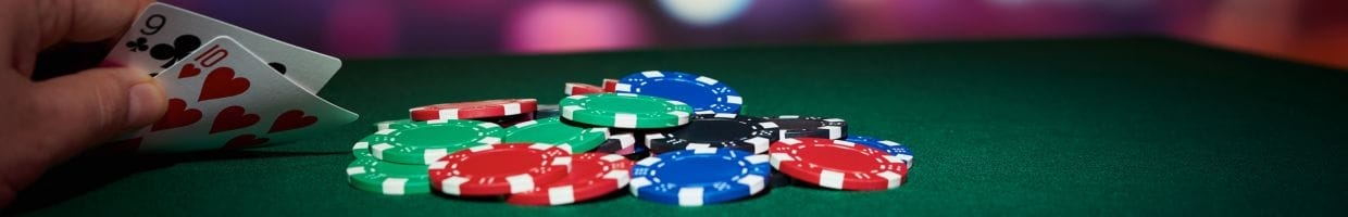 A person holding a nine of Clubs, and a ten of Hearts, sitting at a poker table, with poker chips on the table.