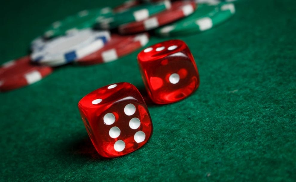 Red dice and casino chips on a green felt table.