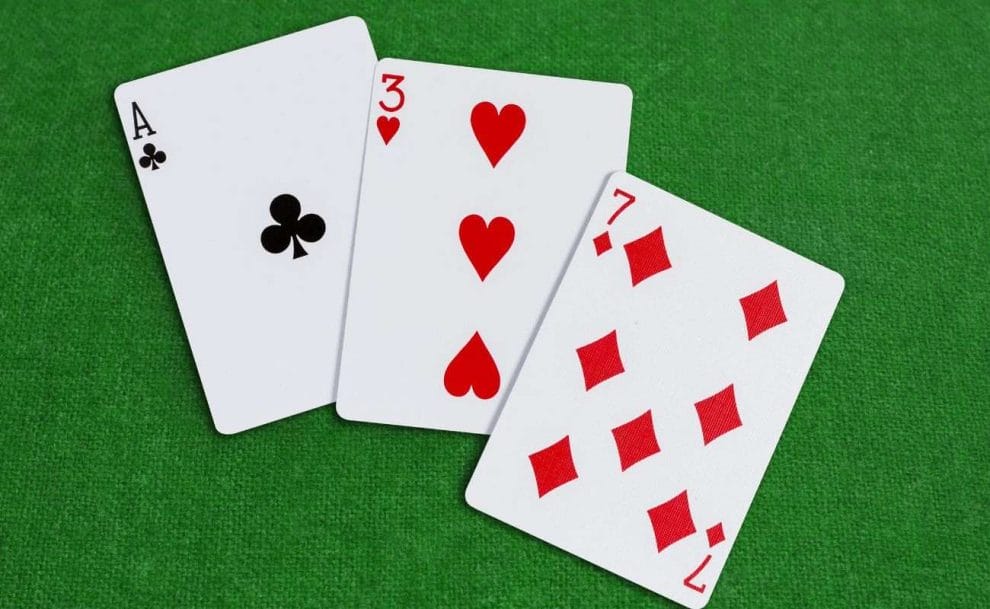 a top view of three playing cards - an ace of clubs, three of hearts and seven of diamonds - on a green poker surface 