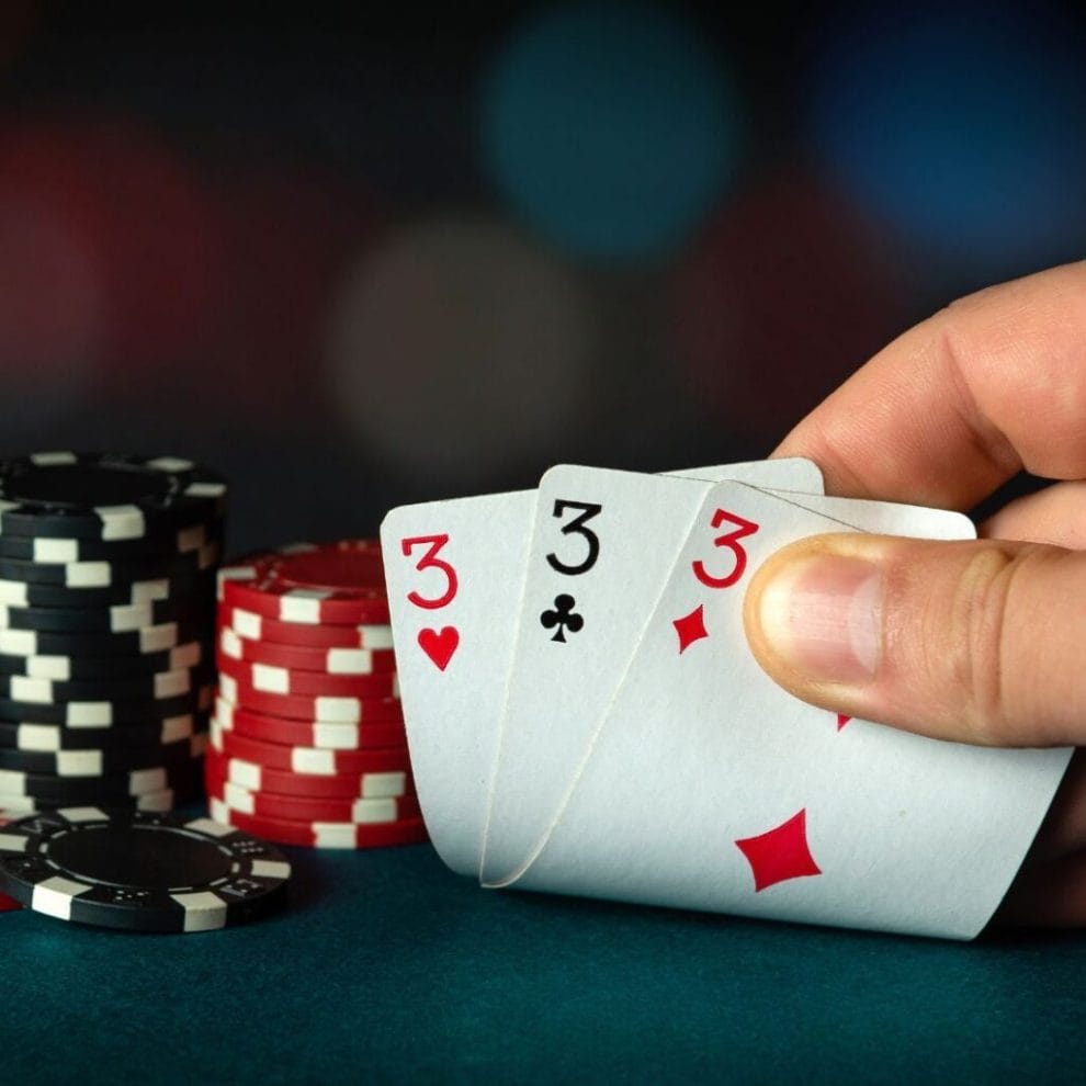 a person checks their three hole cards, a triple three, on a poker table with poker chips stacked on the side
