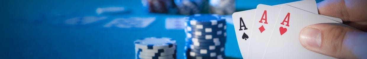 a person checks their three hole cards, a triple ace, on a poker table with poker chips stacked on the table in the background