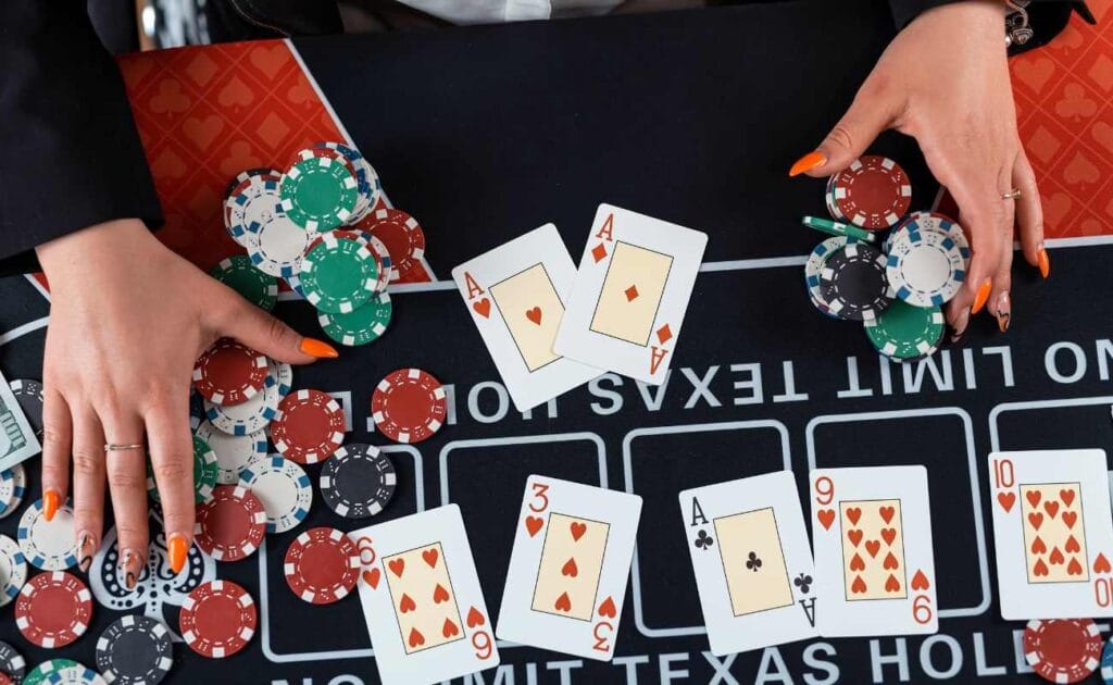 A top-down view of the hands of a female dealer at a No Limit Texas Hold’em poker table with each hand on stacks of poker chips.