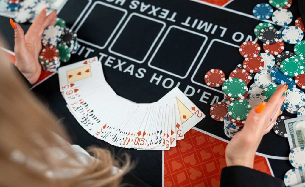 An over-the-shoulder view of a female Texas Hold’em dealer with her hands cupping stacks of poker chips on either side of a fanned-out deck of cards.