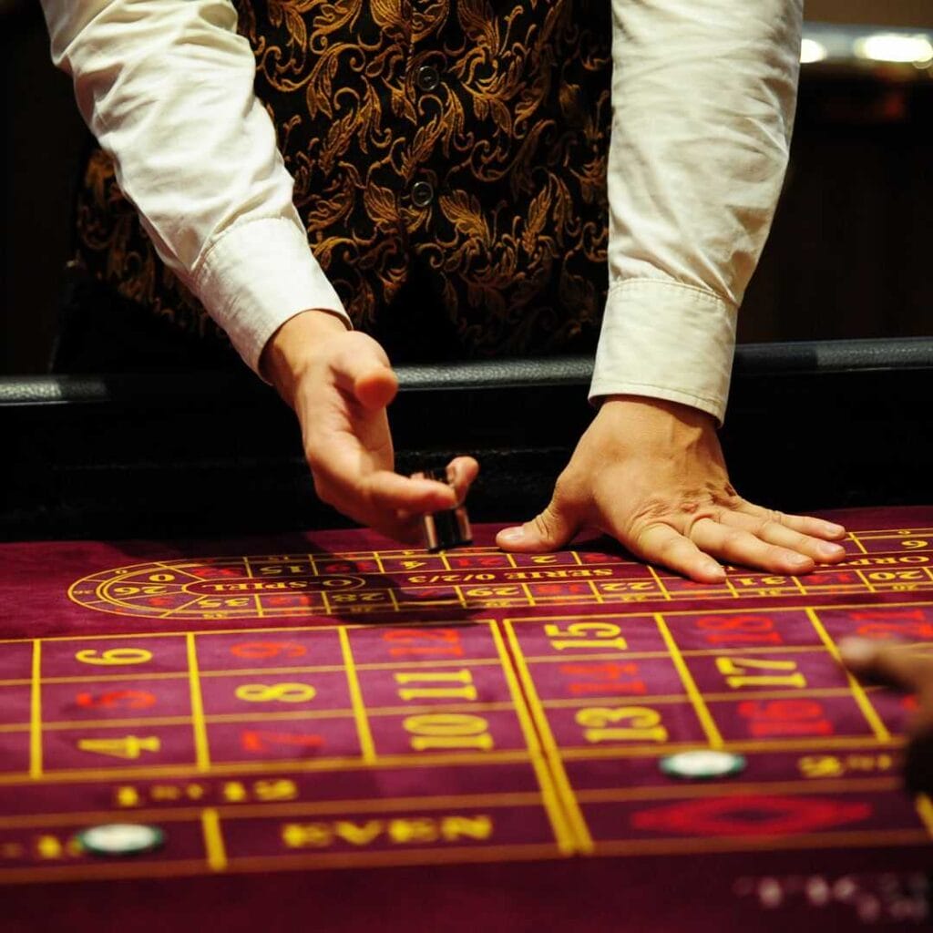 A croupier at a roulette table getting ready to place the marker on the winning number.