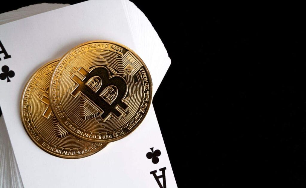 Two gold Bitcoins on top of a deck of playing cards with an Ace of Clubs as the top card with a black background. 