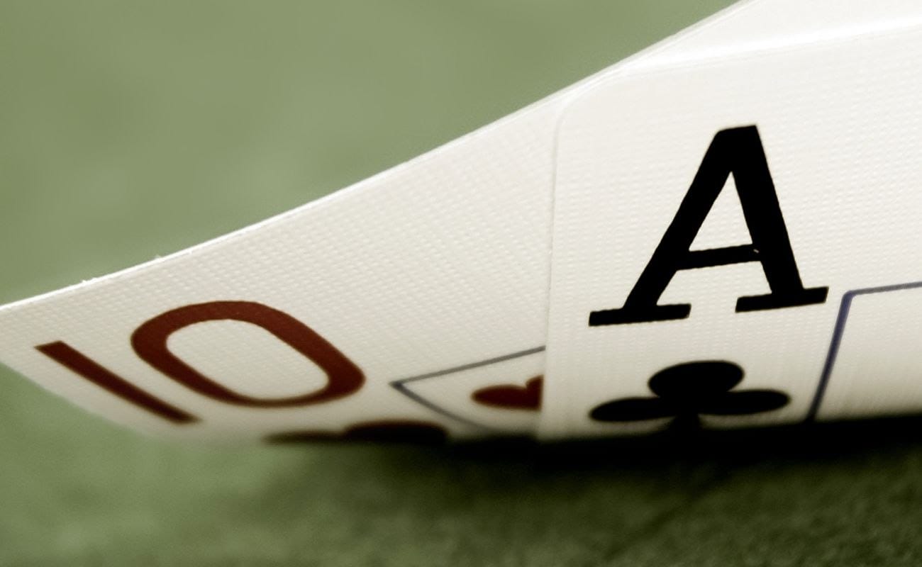 close-up of an Ace of Clubs and Ten of Hearts playing cards being lifted off a green felt poker table to reveal them