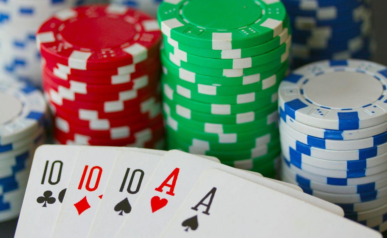 a poker hand of three tens and two aces playing cards being held in front of stacks of poker chips