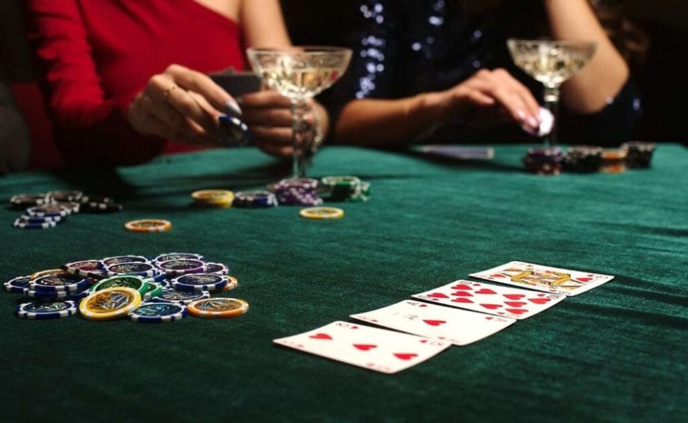 Two female poker players sit at a dark green table and get ready to place their bets. 