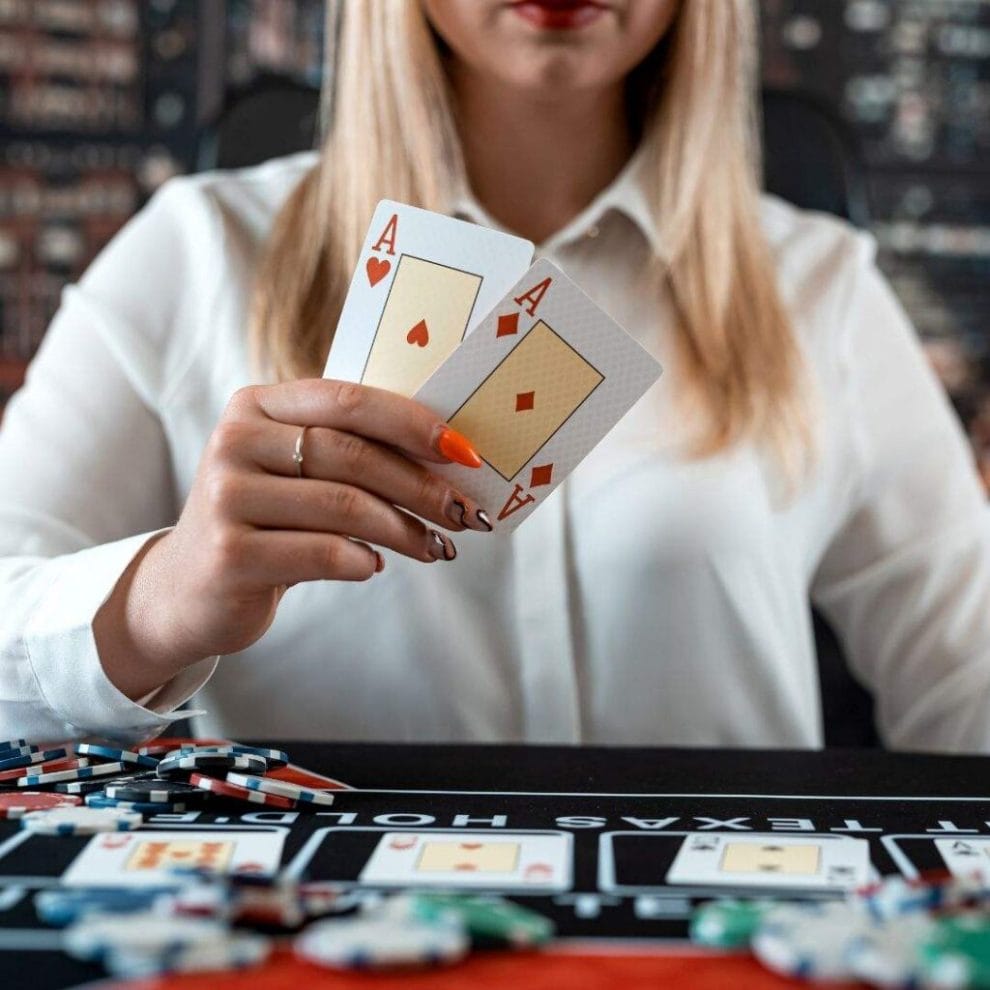 A female poker player at a Texas Hold’em table holds up two Ace playing cards.
