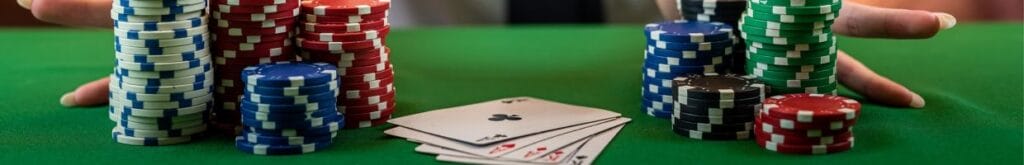 Four stacks of poker chips on each side of four playing cards, all on a green felt poker table.