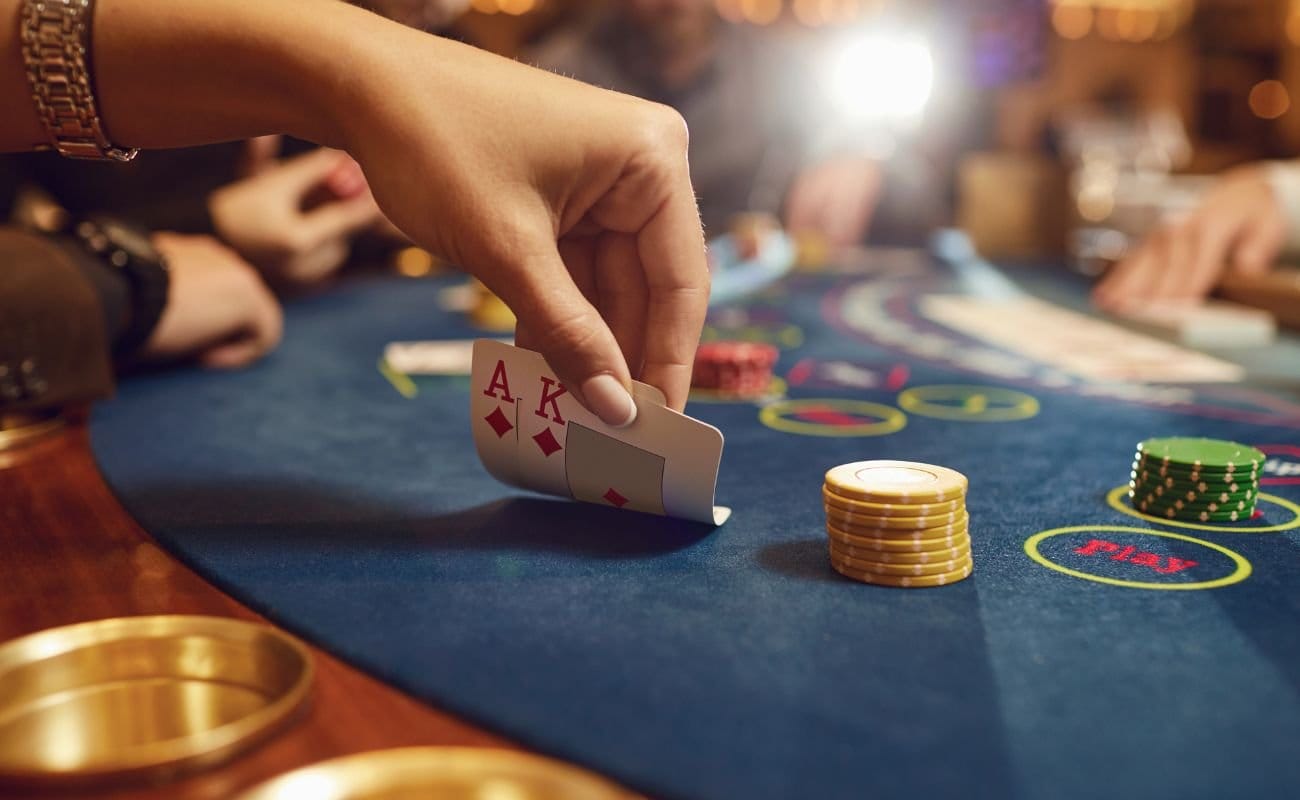 A person sitting at a poker table, revealing a King of Diamonds and an Ace of Diamonds, surrounded by a table of poker chips, and other poker players.