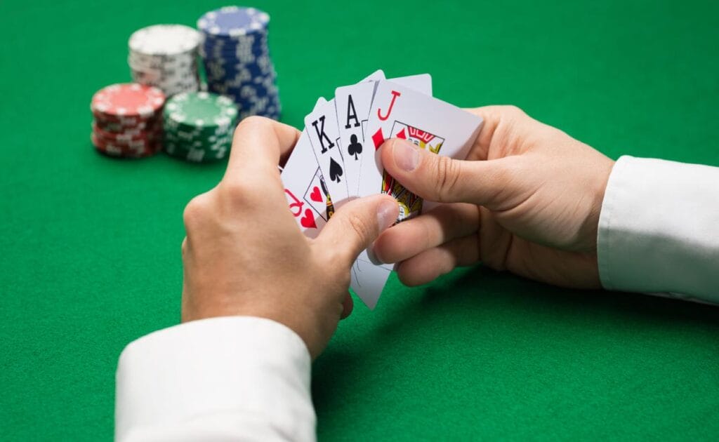 Hands holding playing cards with casino chips on a green felt table.