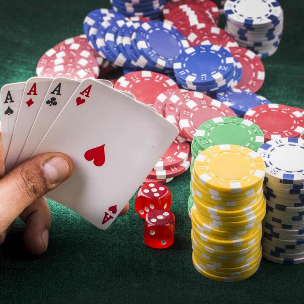 A hand holding four ace playing cards with dice and casino chips on the table.