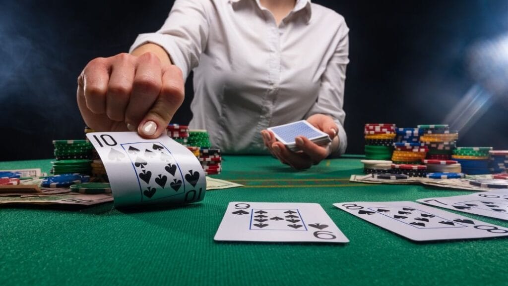 A dealer holding out a ten of Spades card, at a poker table, with playing cards and poker chips arranged on the table. 