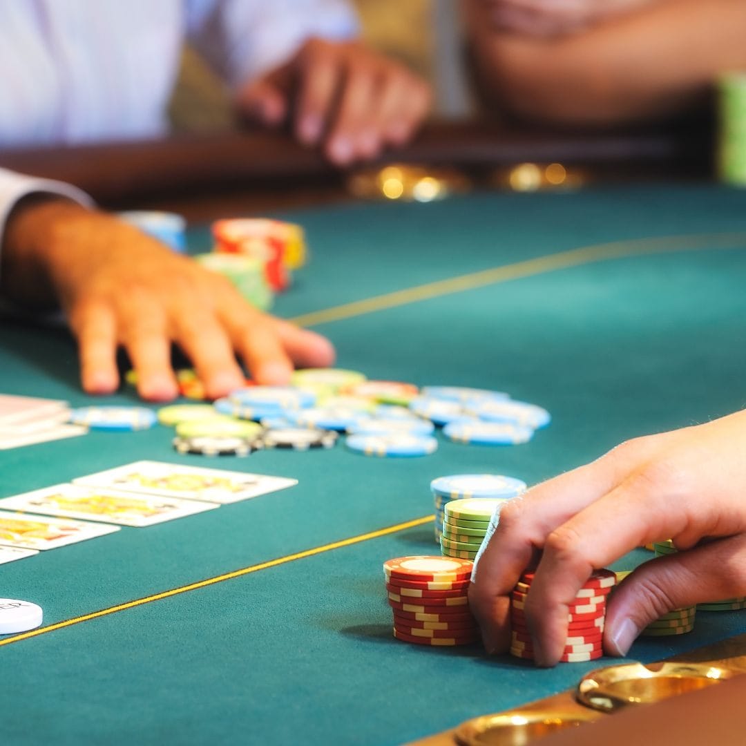 A person, and a poker dealer sitting at a poker table with playing cards, and poker chips on the table.