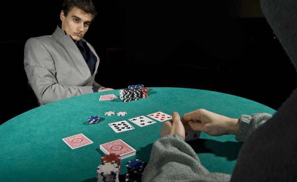 Two men dressed in grey sit at a round table and play a game of poker.