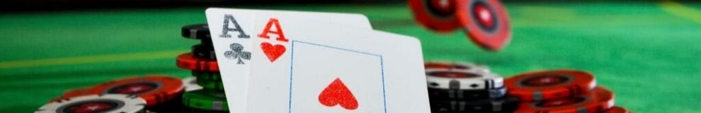 An Ace of Clubs and an Ace of Hearts balancing against poker chips on a green felt poker table.