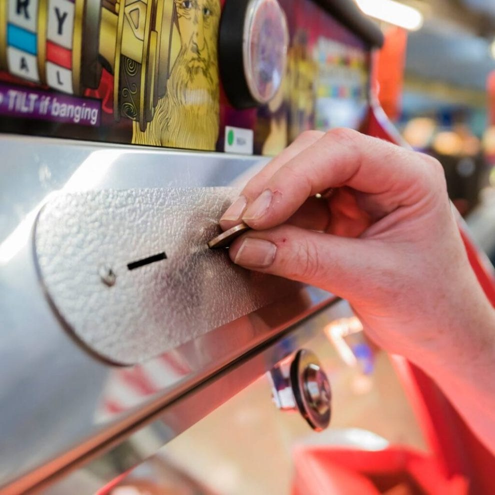 A hand inserting a coin into a penny slot machine.