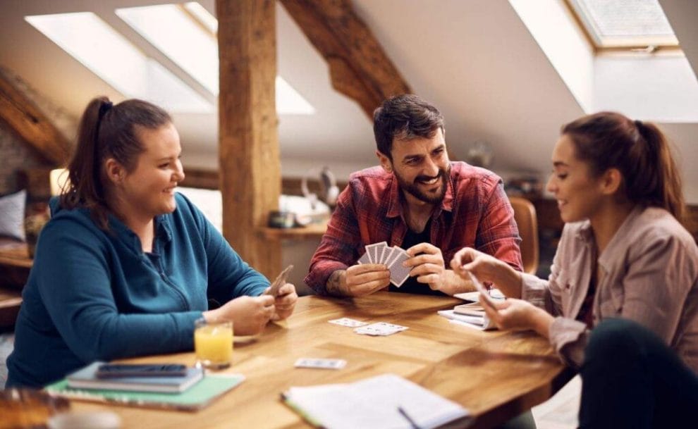 A group of friends playing poker around a wooden table, with no poker chips.