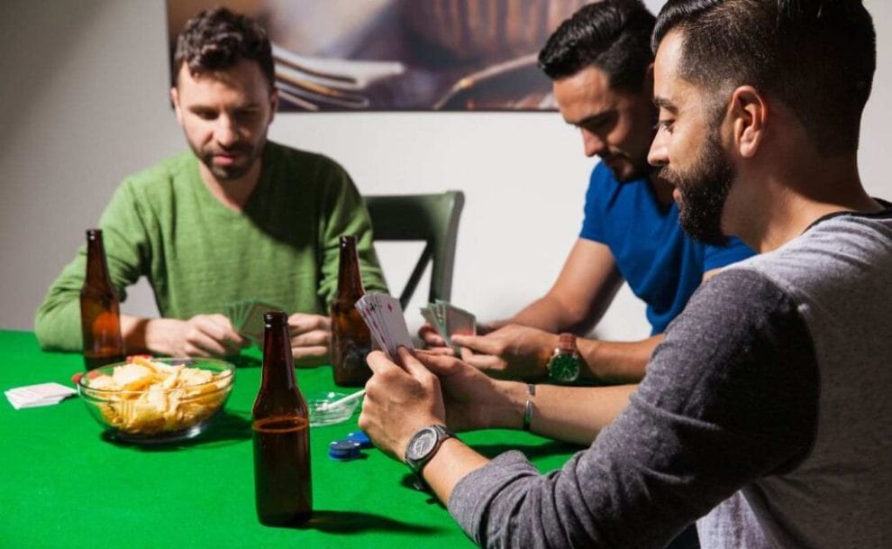 Three men playing poker at home with a bowl of chips and beer on the table.