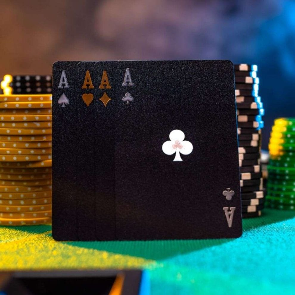 Four black Ace cards, one of each suit, balancing against stacked poker chips on a green felt table.