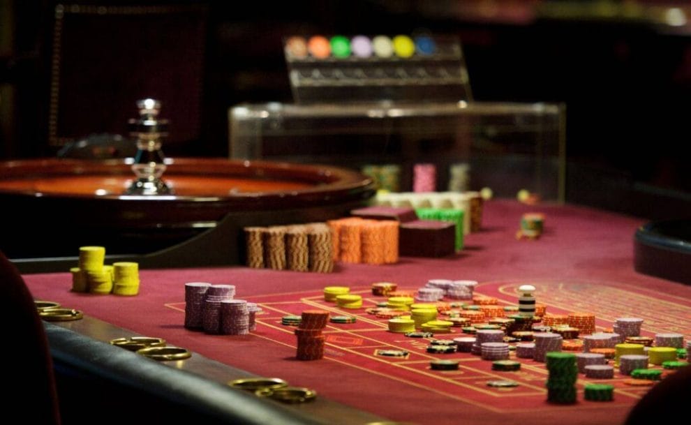 A photograph of a roulette table with casino chips stacked next to the wheel, down the side of the table, and on each number on the table.