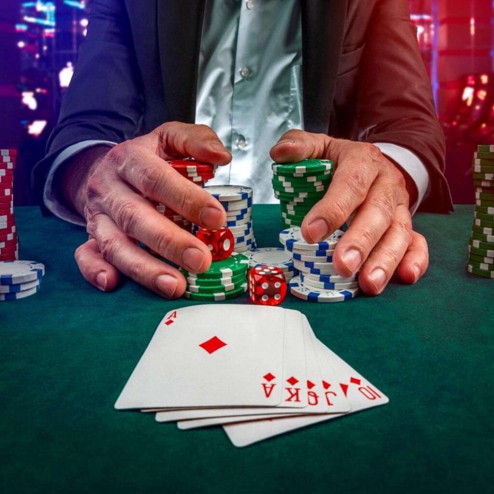 A closup of a poker player’s hands cupping his winnings and two red six-sided dice on a green felt poker table with a straight poker hand in front of him.