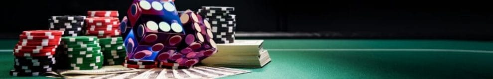 Small stacks of poker chips, two six-sided dice, a stack of cash, and cash fanned out on a green table.