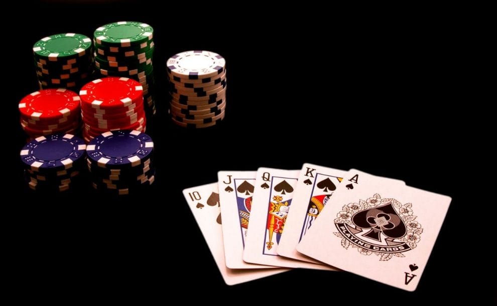 A Royal Flush in the clubs suit and seven stacks of poker chips on a black table.