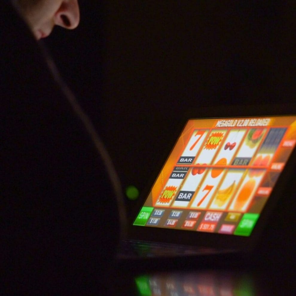 A person sitting in a dimly lit room, playing an online slot game on a laptop.