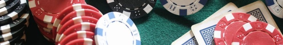 A close up of poker chips, and playing cards, arranged on a poker table.