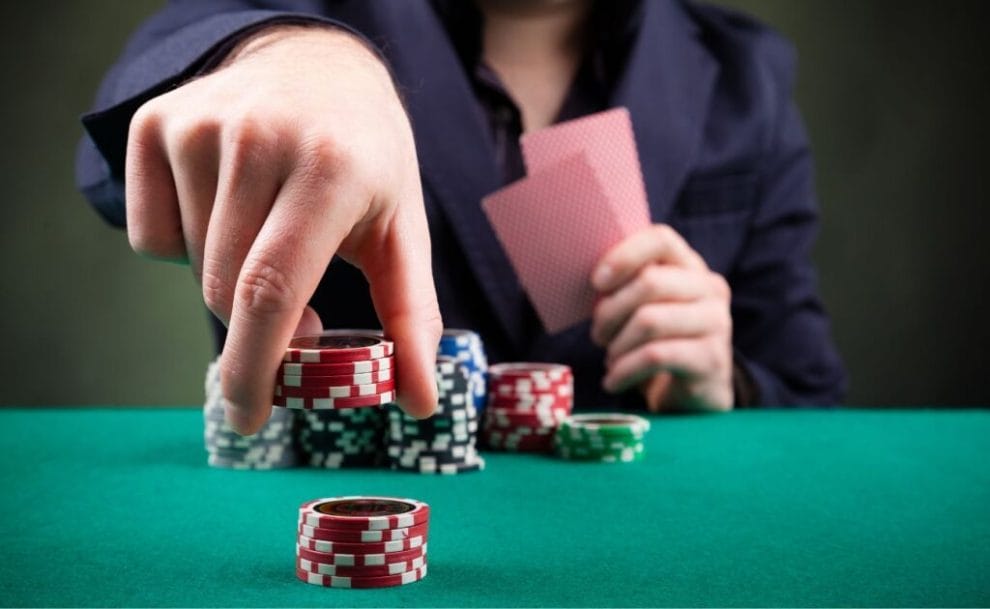 a person placing a stack of red poker chips down on a green felt poker surface while holding two playing cards in their other hand