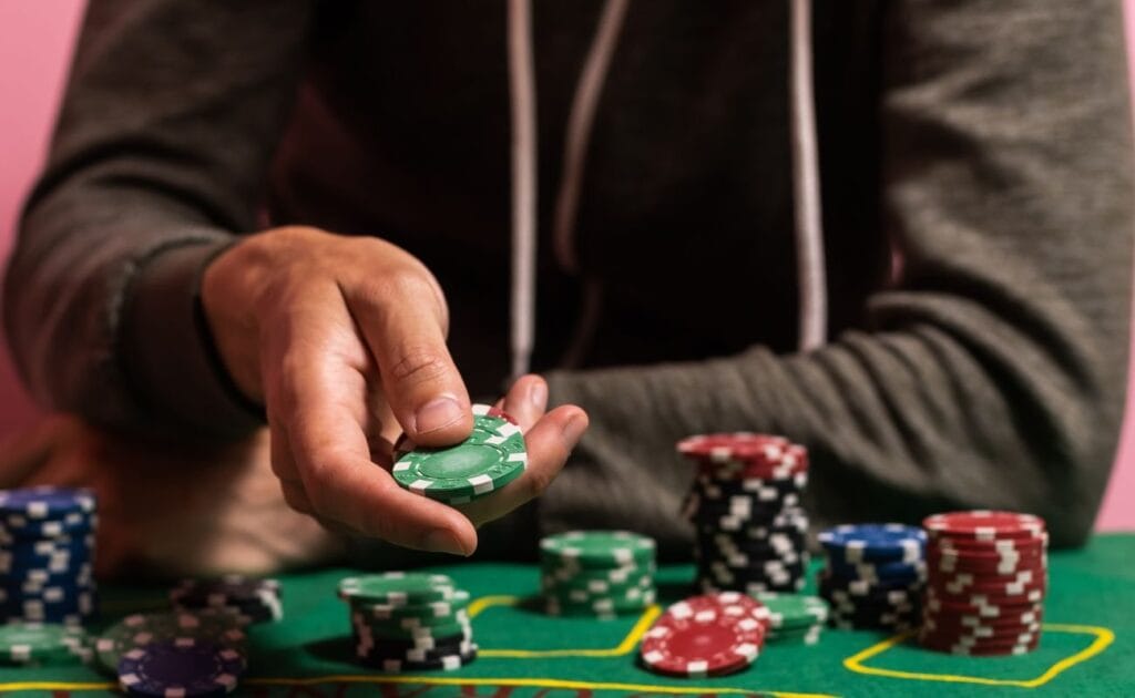 a person holds out poker chips over a green felt poker table with other stacks of poker chips on it 