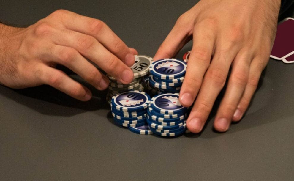 a person’s hand covering stacks of poker chips on a poker table 