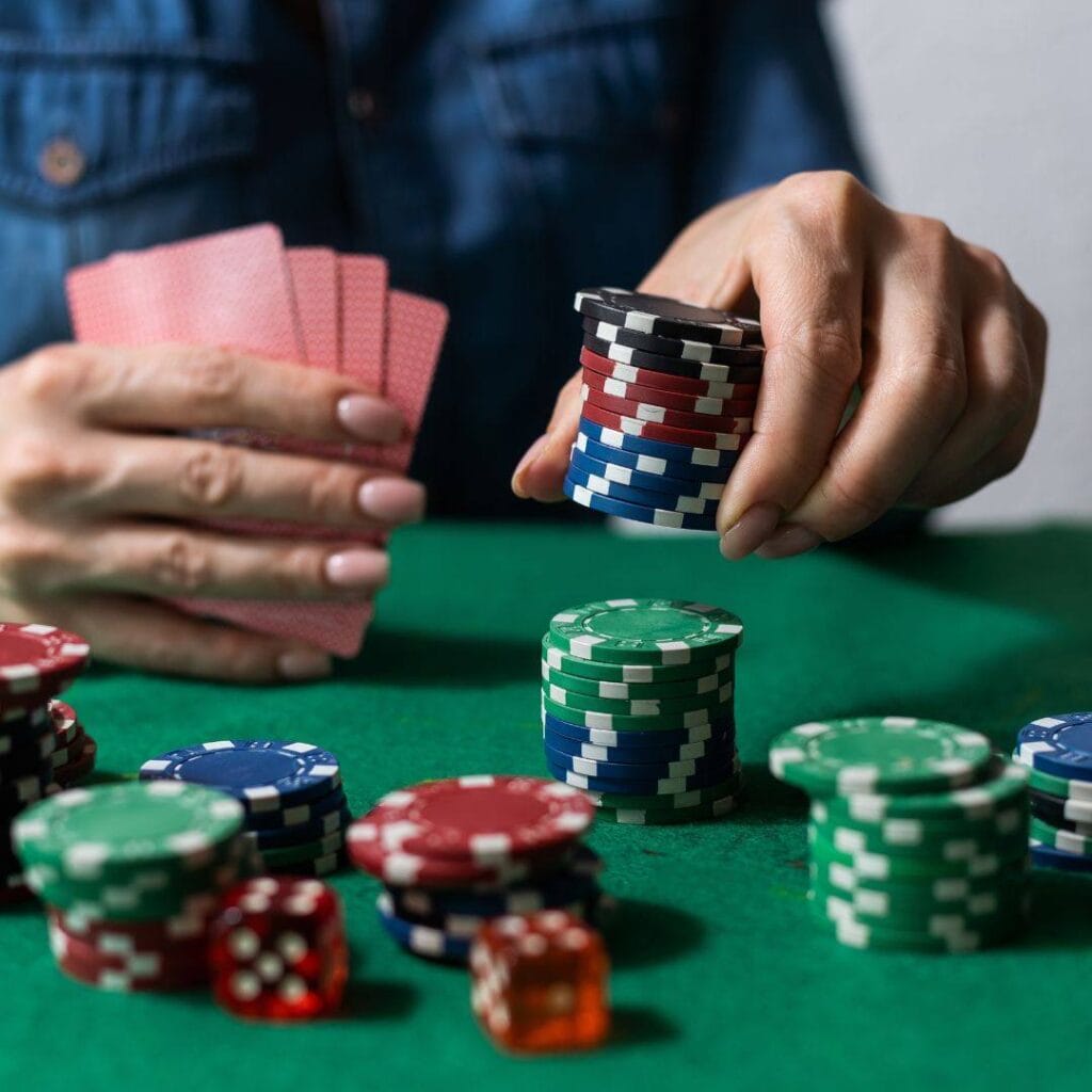 a person holds playing cards in their right hand while placing a stack of poker chips down on a green felt poker surface with their left hand