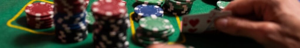 a person checks their hole cards on a green felt poker table with stacks of poker chips in front of them