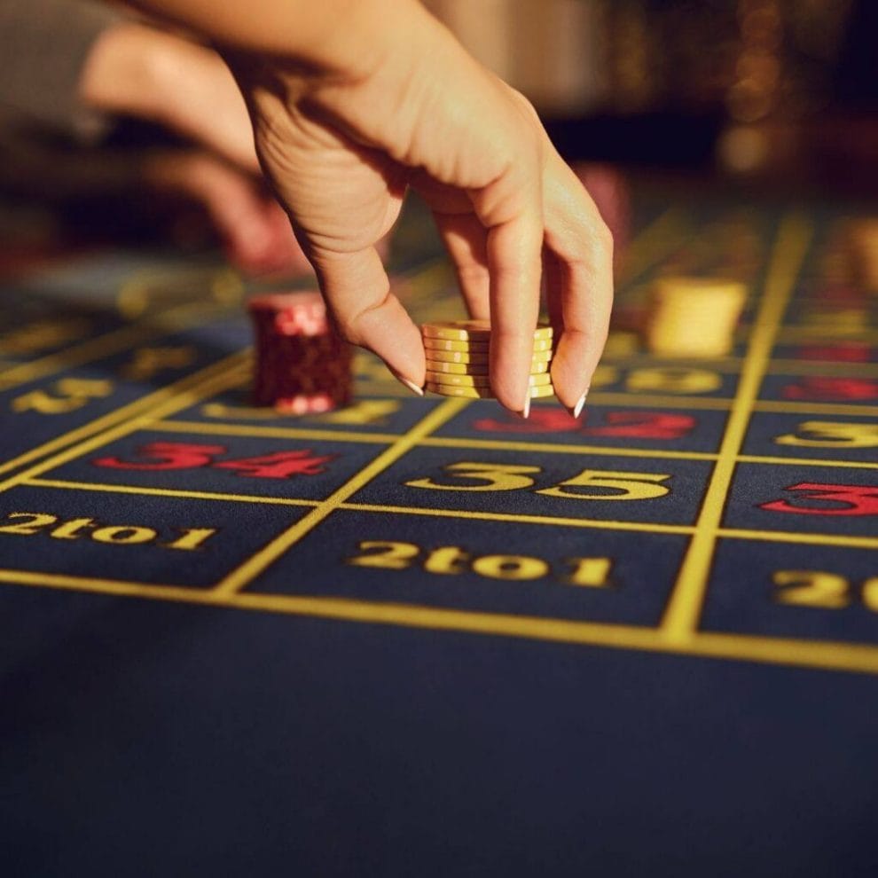 a person placing a stack of yellow poker chips down on a roulette table in a casino