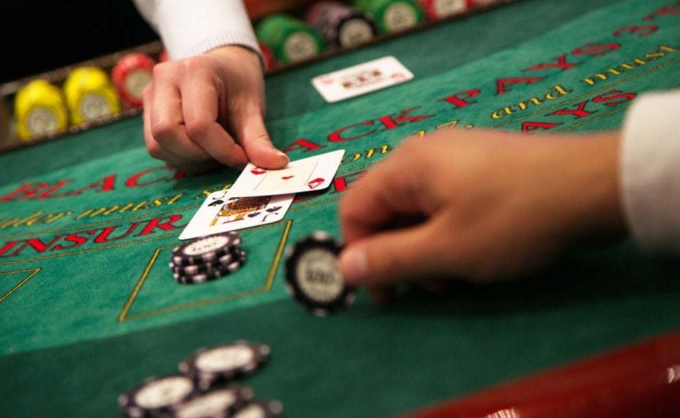 A croupier puts cards on the table, while a player passes over a casino chip