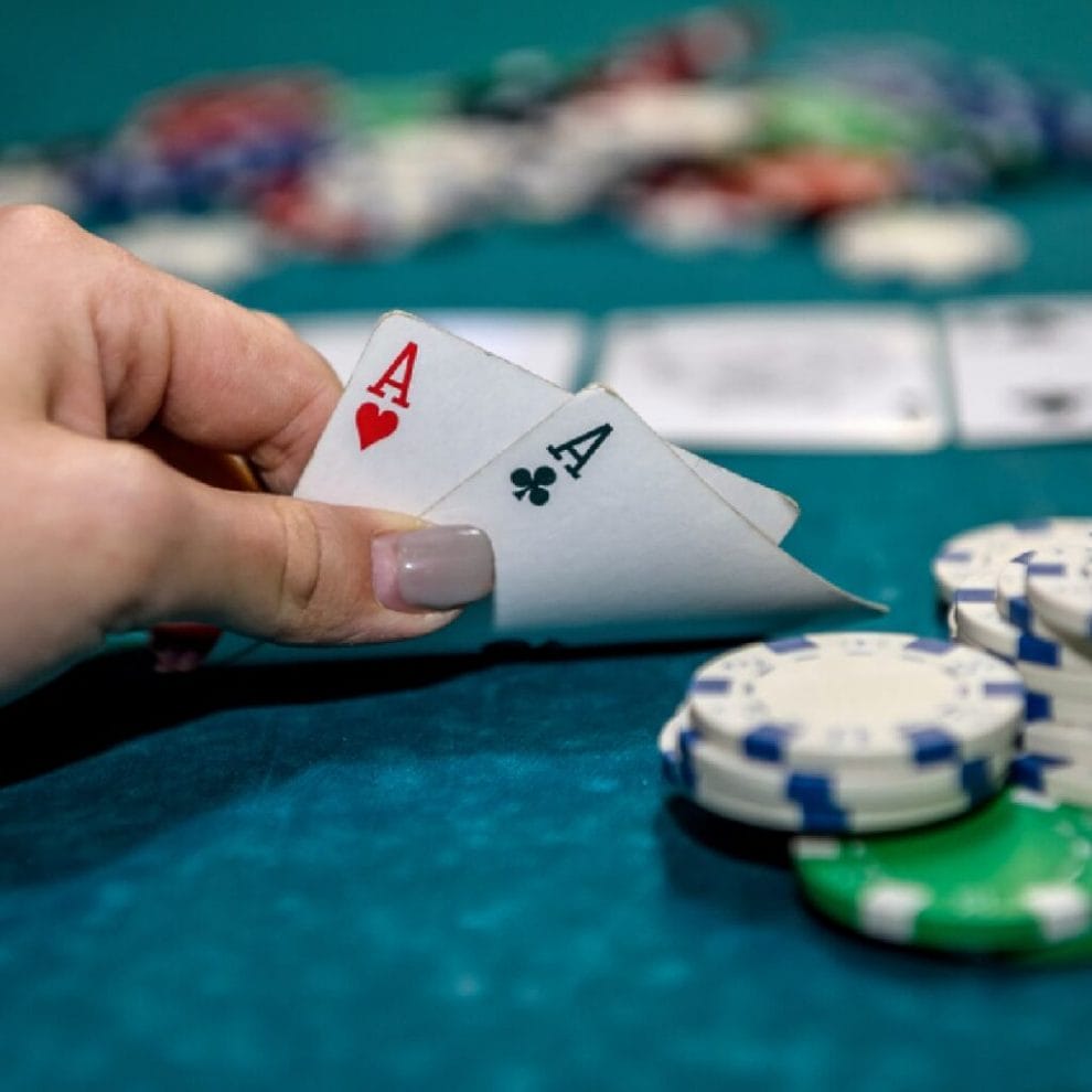 A woman holds a hand of two aces next to some poker chips