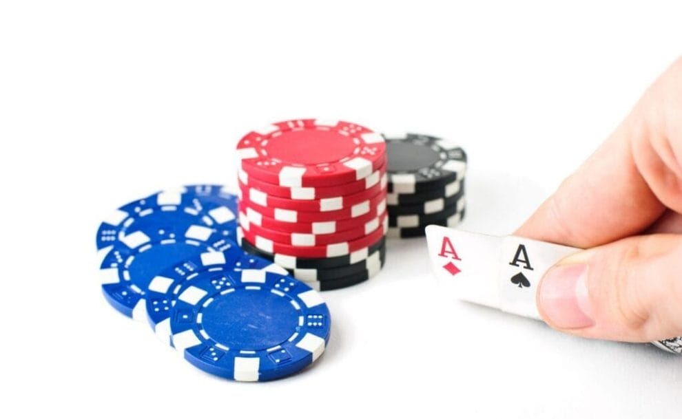 Three small stacks of poker chips and a hand holding two Ace playing cards on a white background.