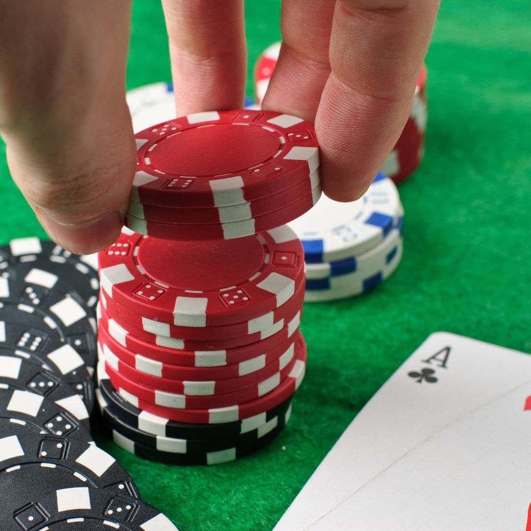 A closeup of a hand taking a few poker chips off the top of a small chip stack next to two Ace playing cards on a green felt table.