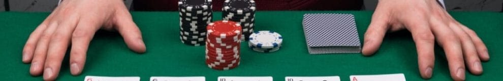 A dealer’s hands, casino chips and playing cards on a green felt table.