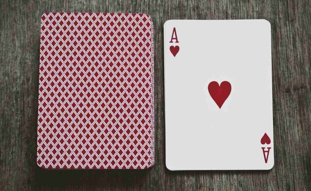 A stack of cards facing down to the left, one ace of hearts facing up to the right.
