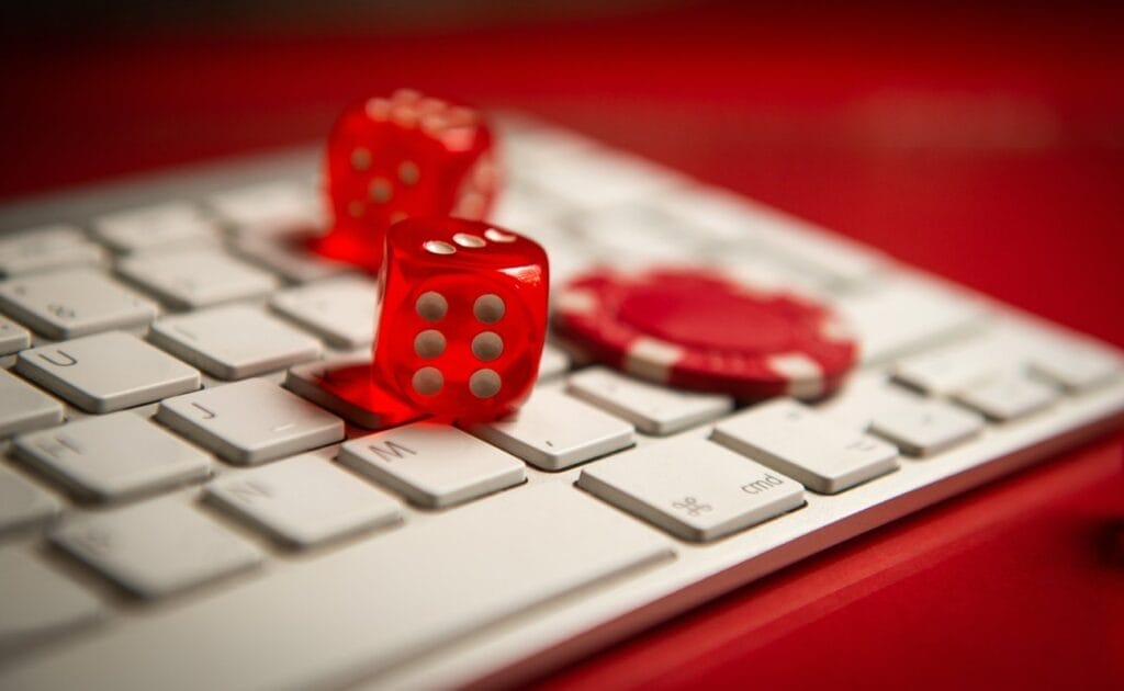 Two red dice and a red poker chip, atop a white keyboard with a red background.