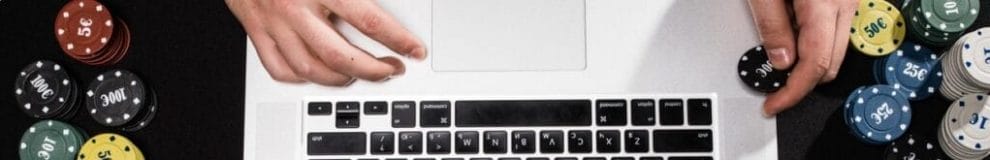 A birds eye view of a pair of hands on a laptop keyboard, with stacks of poker chips either side.